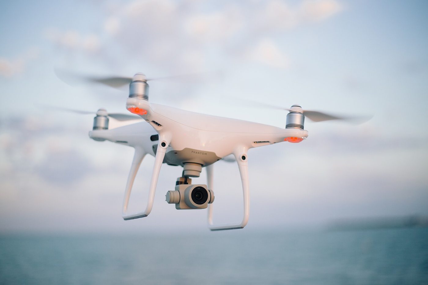 Camera drone hovering over calm water at dusk with its gimbal camera ready
