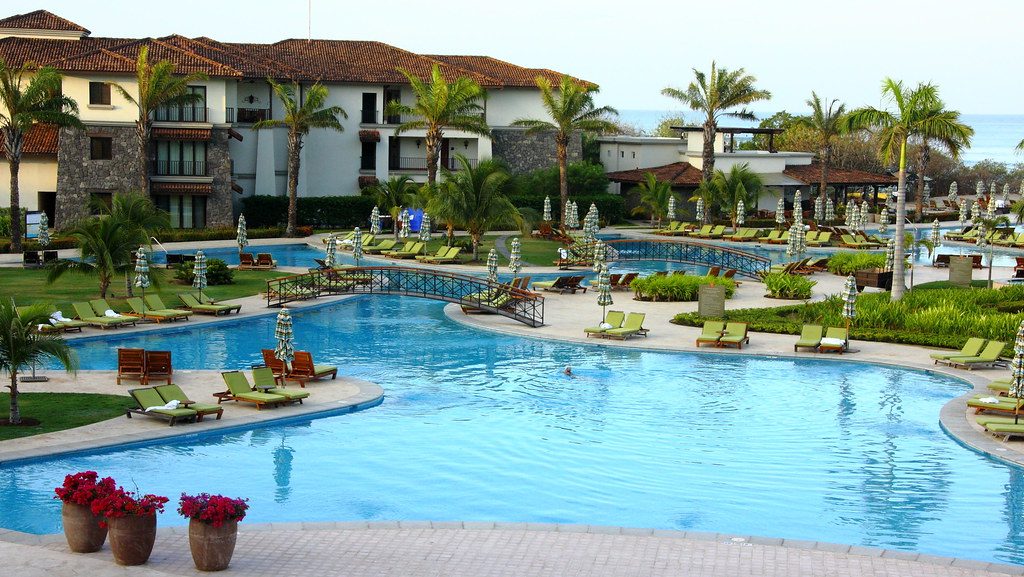 Resort pool with palm trees and lounge chairs near the ocean in Guanacaste